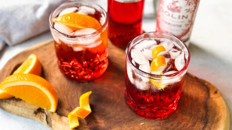 Aerial view of Americano cocktails in old fashioned glasses on a cutting board with Dolin and orange slices.