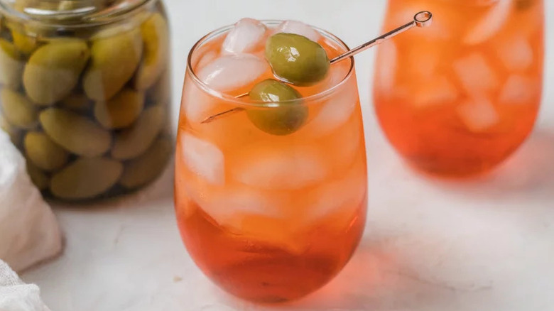 A stemless glass of Aperol spritz with olive garnish.