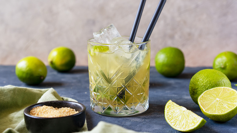 Caipirinha cocktail in rocks glass, surrounded by fresh limes