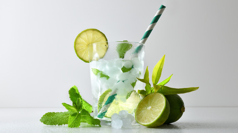 Mojito cocktail surrounded by fresh lime halves and mint sprigs