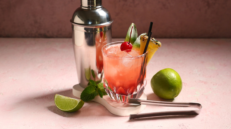 Mai tai cocktail next to metal shaker and fresh limes