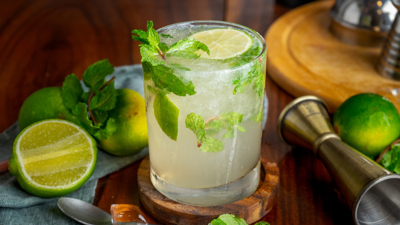 Mojito cocktail surrounded by fresh limes and mint sprigs
