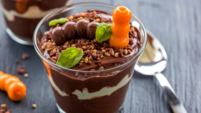 dirt pudding in a cup with candy on top with spoon against black background