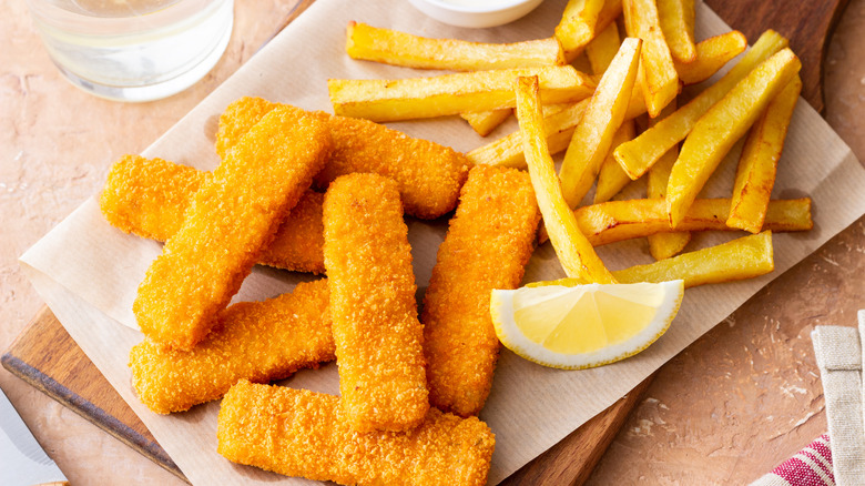 fish sticks and fries on a paper against brown background