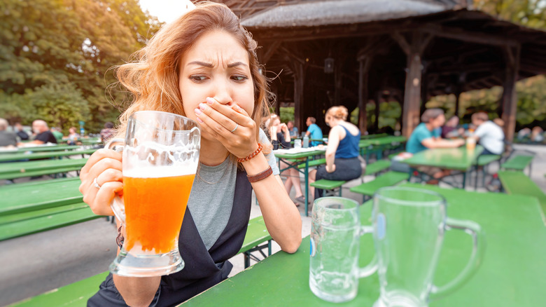 Woman outside at table covering her mouth and looking disgusted at beer