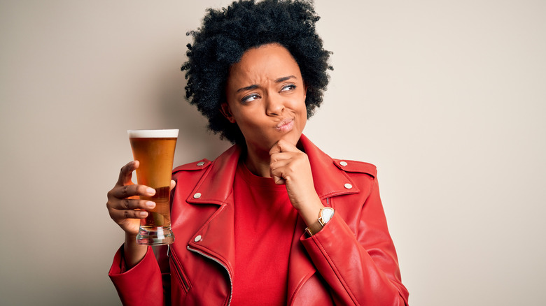 Woman in leather jacket with pint of beer looking uncertain