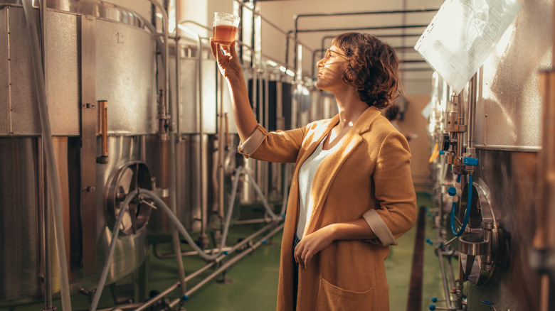 Woman looking at beer in glass in brewery