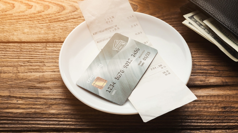 Credit card and food bill on app plate on table near wallet