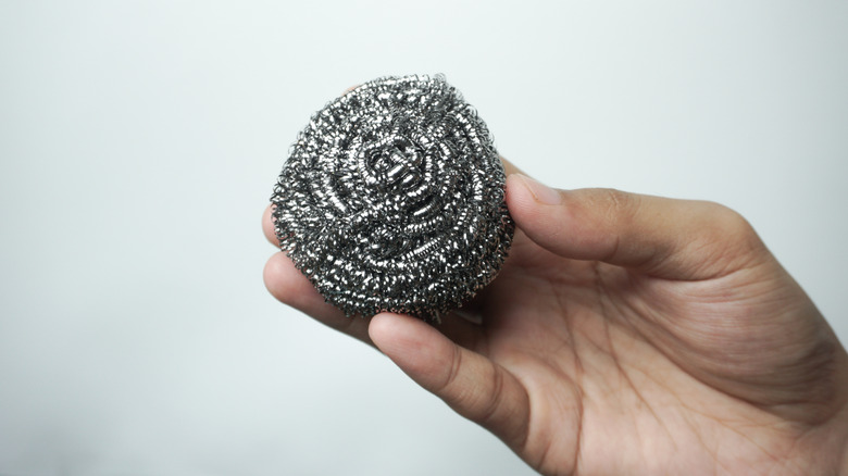 Hand holding a coiled metal pot scrubber, against a neutral background