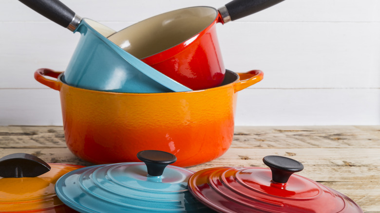Enameled Le Creuset cookware in multiple colors, stacked haphazardly together on a rustic wooden countertop