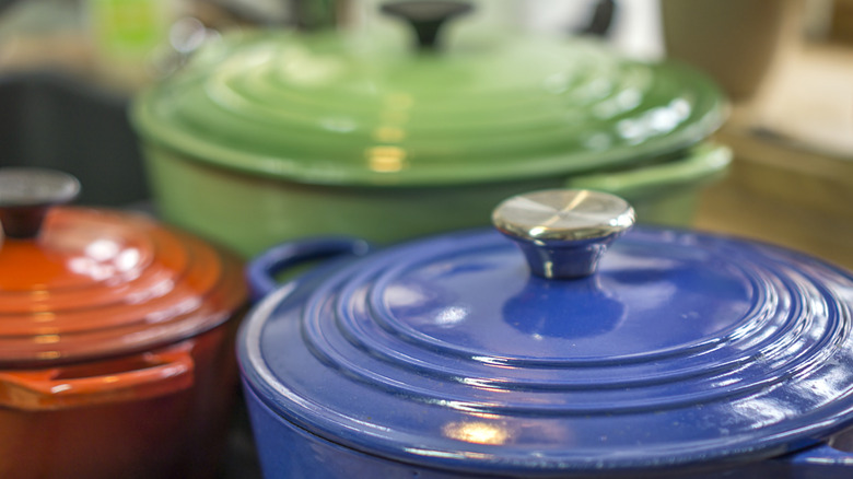 Colorful enameled Dutch ovens in blue, orange, and green, with lids boasting both stainless steel and black plastic knobs
