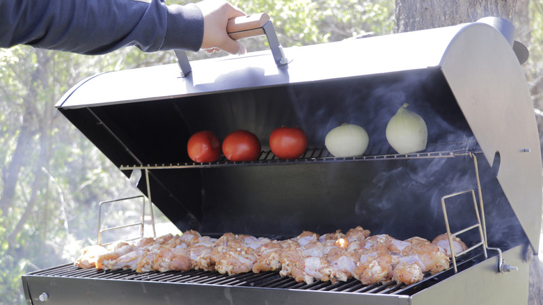man's arm lifting the lid of a grill filled with chicken pieces