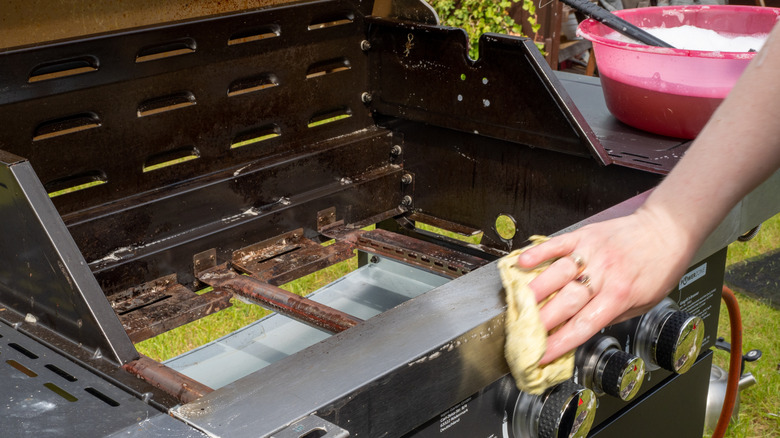 woman's hand running a cloth along the front of a gas grill