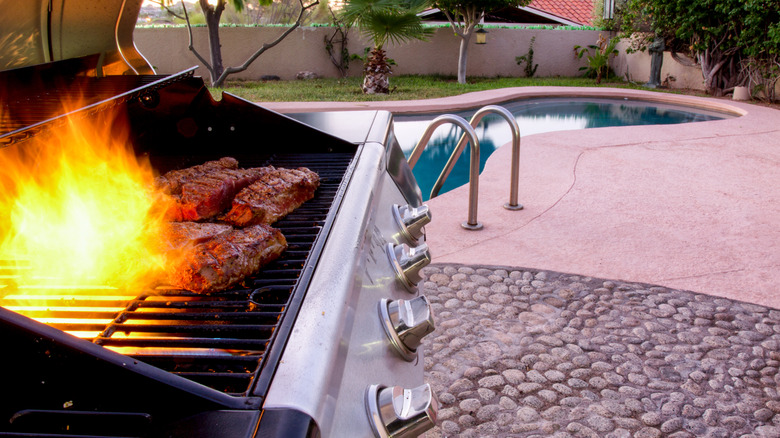a flame springing up between strip steaks on a gas grill