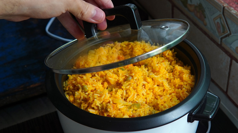 Hand lifting the lid of a rice cooker