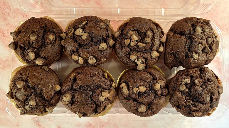 Top-down shot of triple chocolate Costco muffins in container on pink surface