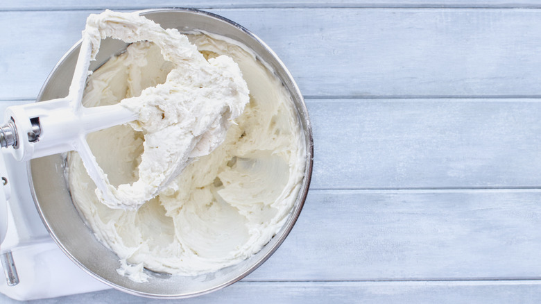 Electric mixer filled with homemade cream cheese frosting on a wooden tabletop