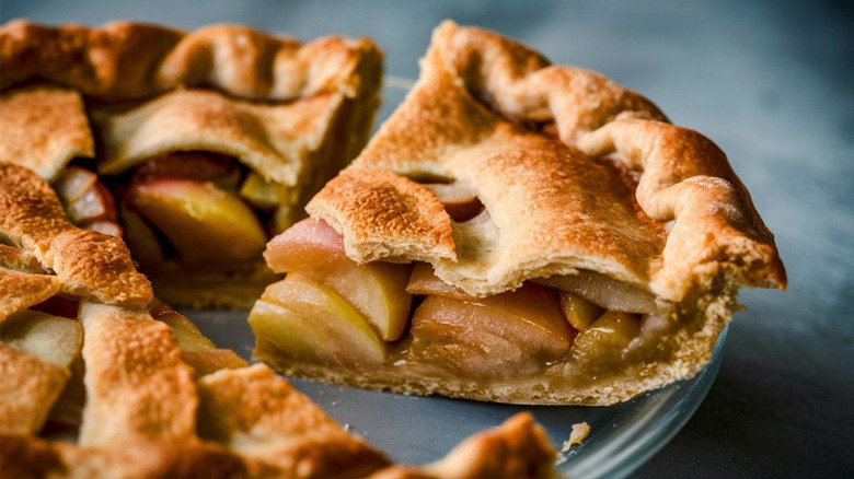 Classic apple pie and slice with tender apples on a glass serving dish