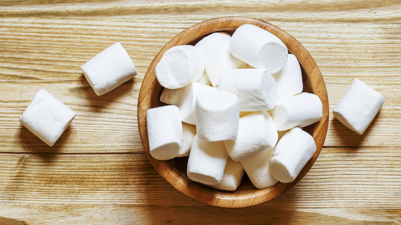 Large marshmallows in a wooden bowl and on a wooden tabletop
