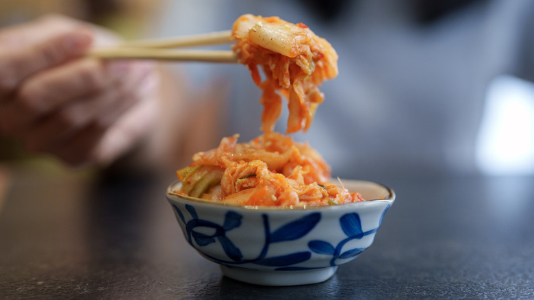 Lifting kimchi from blue and white patterned bowl with chopsticks