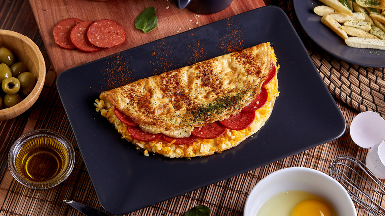 Pepperoni omelet on black rectangular plate,  sprinkled with dried herbs and spices