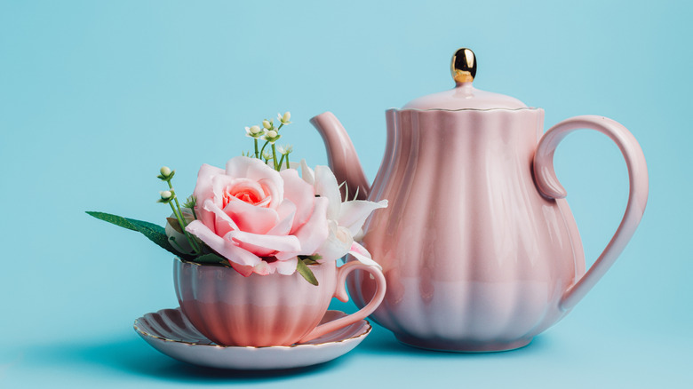 A pink teapot and coffee cup filled with flowers against a blue background