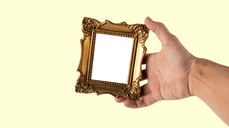 Hand holding a miniature golden frame against an isolated yellow background