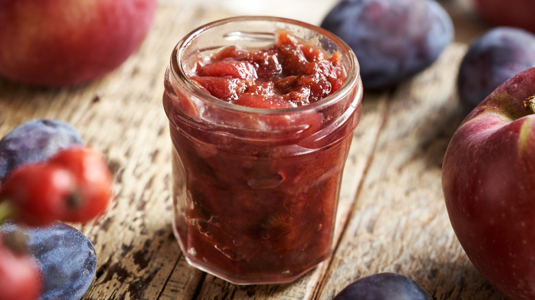 Plum chutney in a glass jar surrounded by fruit
