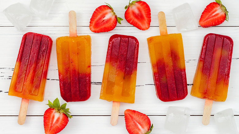 Orange and red paletas surrounded by fresh fruit
