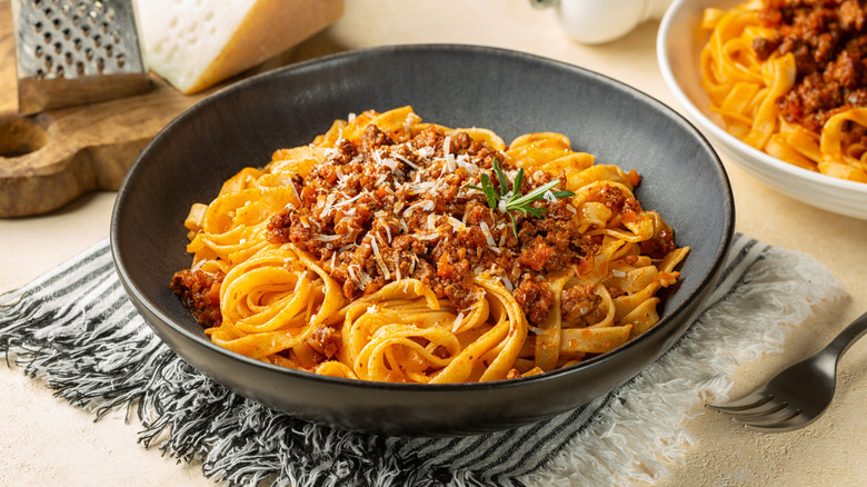Tagliatelle and meat ragu in a black bowl, topped with parmesan served in a dark bowl with another serving in the back