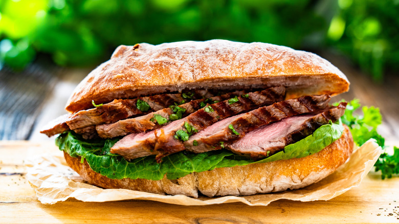 A close-up image of a steak sandwich on a long roll with meat slices inside
