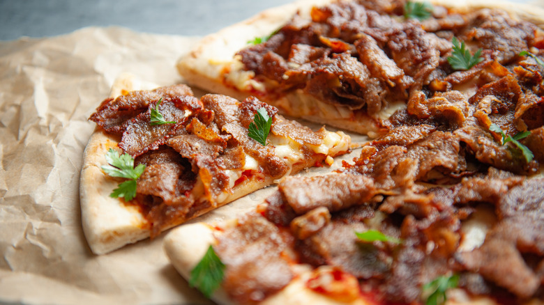 A close up of a beef-topped pizza on parchment paper with one slice cut out