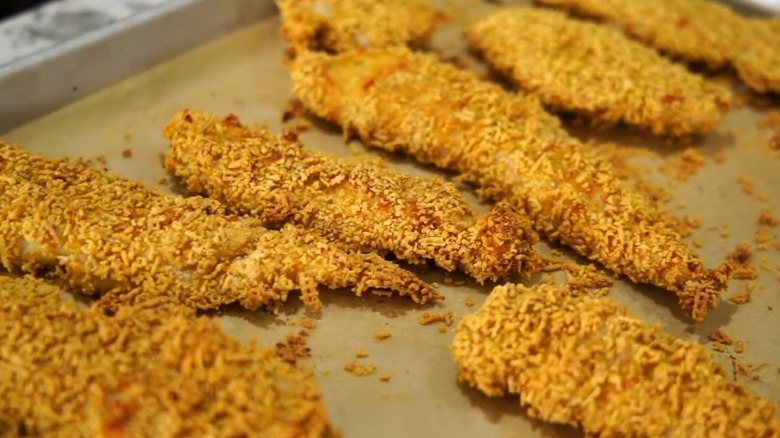 Chex Mix-coated chicken tenders on baking sheet