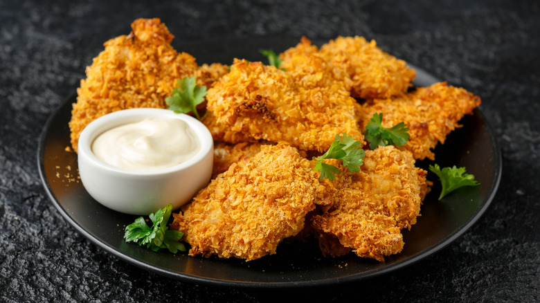 Cornflake-crusted chicken pieces on plate with pot of creamy dip