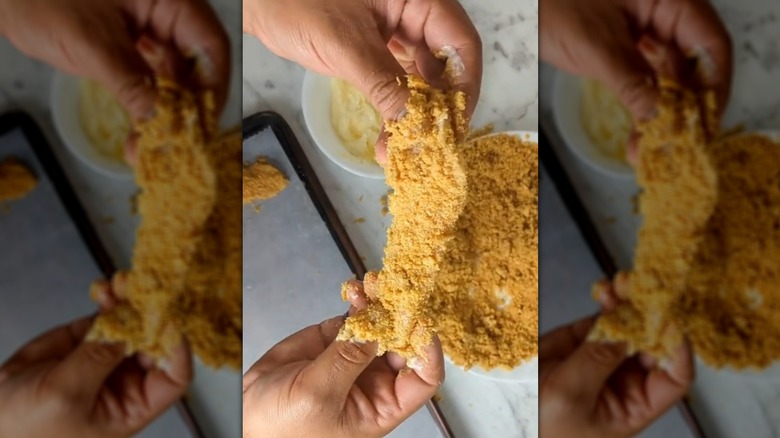 Hands holding chicken strip coated in pork rinds