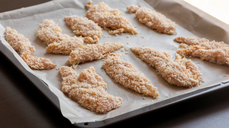 Shredded coconut-coated chicken tenders on parchment-lined baking sheet