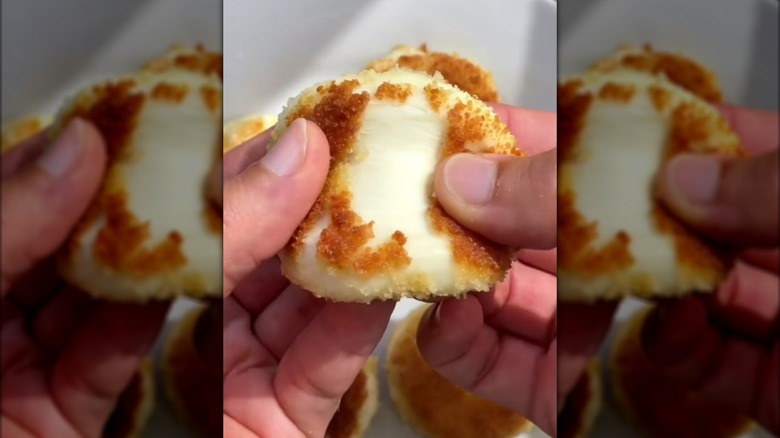 Hands pulling apart crispy breaded Babybel cheese