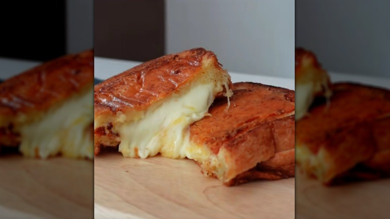 Sliced grilled cheese on wooden board with melty cheese spilling out