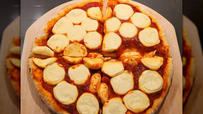 Babybel-topped pizza on wooden board, sliced into quarters