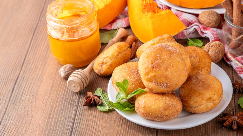 A plate of pumpkin donuts surrounded by pumpkin chunks and other ingredeints