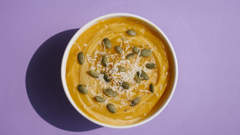 Topview of a bowl of pumpkin soup on a purple background