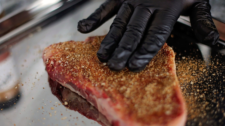 Gloved hand adding dry rub to beef steak