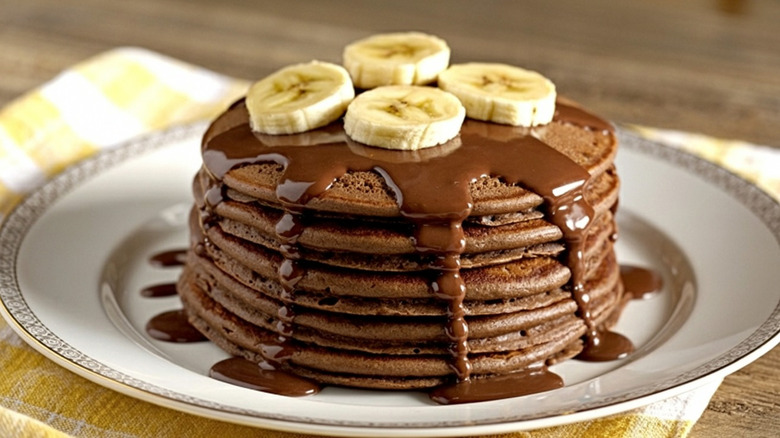 Stack of chocolate pancakes topped with chocolate sauce and sliced banana