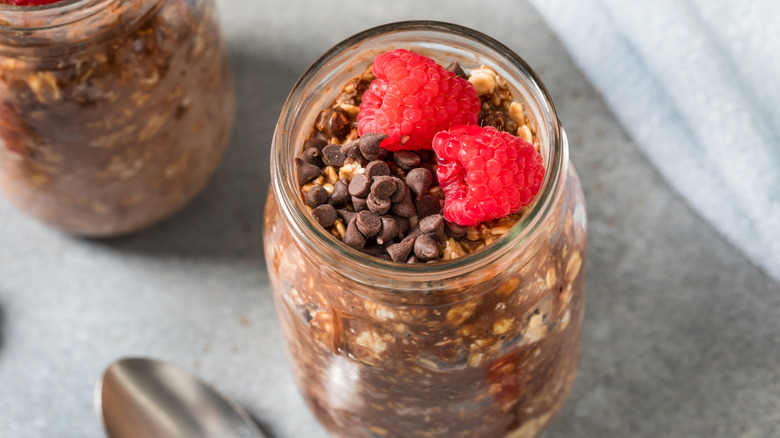 Jar of chocolate overnight oats topped with fresh raspberries and chocolate chips