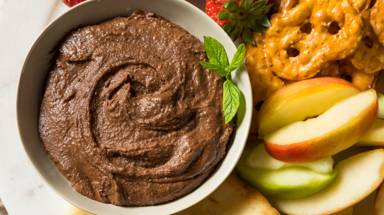 Bowl of chocolate hummus served with sliced apples and pretzels