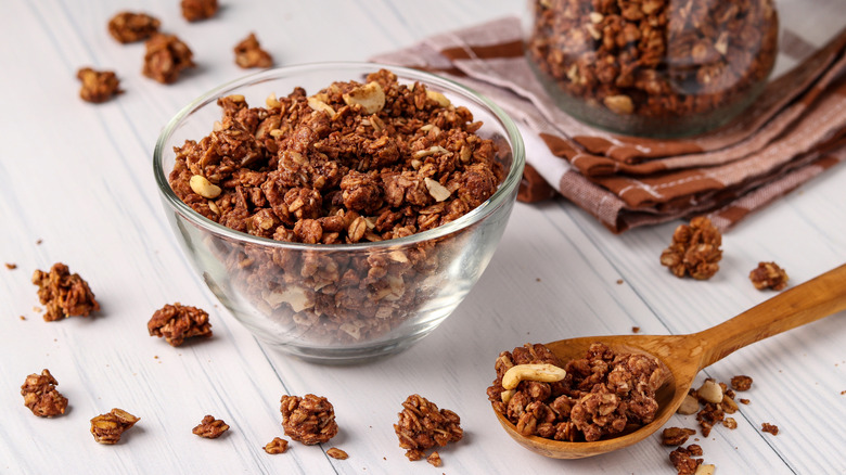 Chocolate and nut granola in glass bowl next to wooden spoon