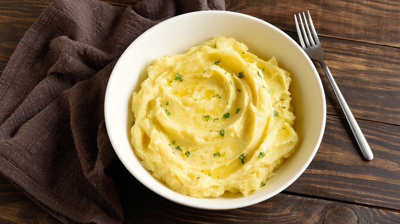 Mashed potatoes in white bowl, garnished with fresh herbs