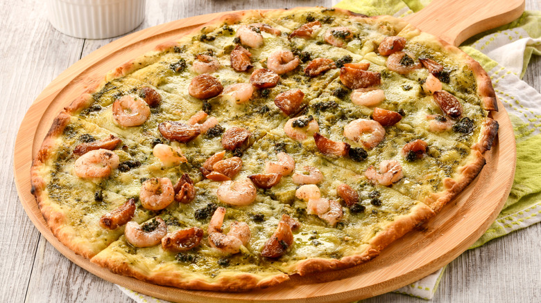 Pizza topped with pesto, shrimp, and roasted garlic cloves on wooden serving board