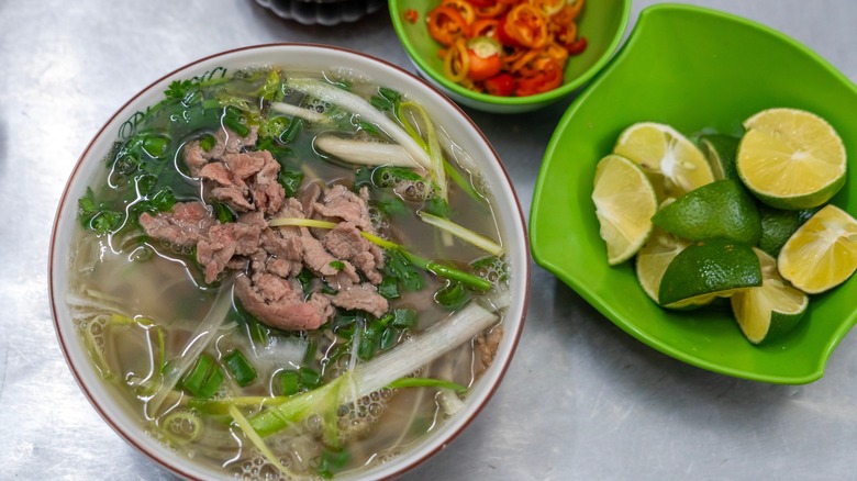 Topview of a bowl of pho next to fresh lime and chile