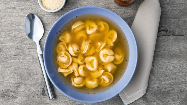 Topview of a blue bowl of tortellini soup and a spoon